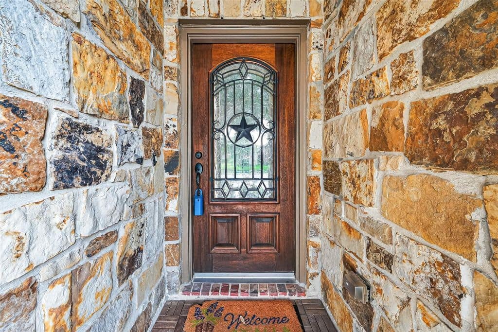 Stone entryway and a wooden front door with a Texas star window on a Houston home