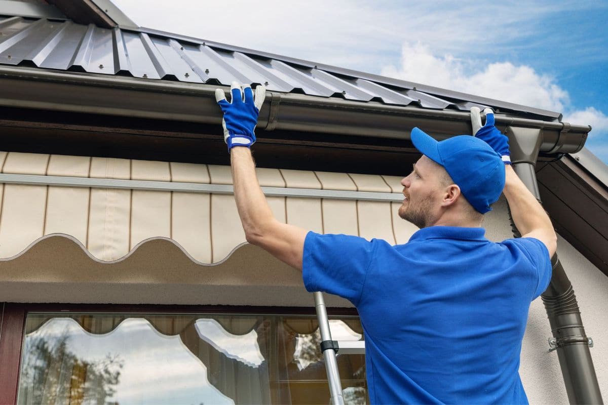 Technician in blue installing a gutter along a metal roof edge
