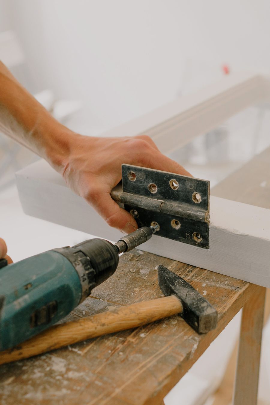 Handyman driving screws into a door hinge with a cordless drill