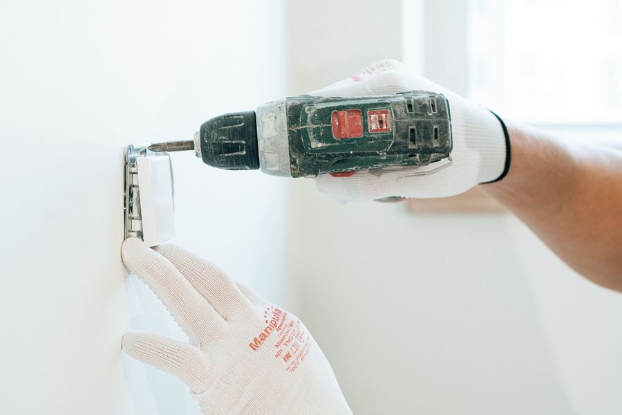 Worker in gloves driving a screw to mount a light switch on a wall
