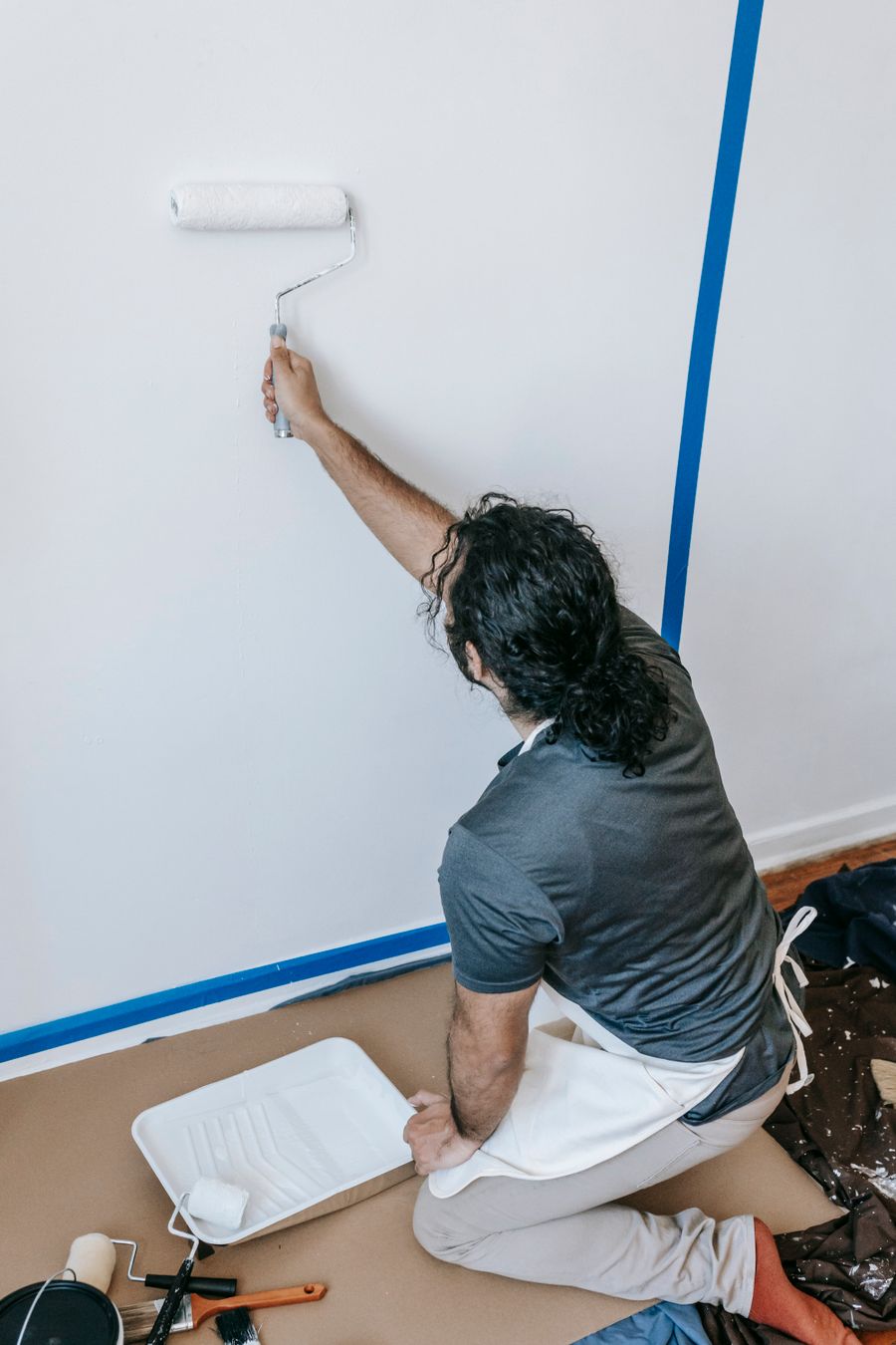 Painter rolling fresh paint on a taped-off interior wall over a covered floor