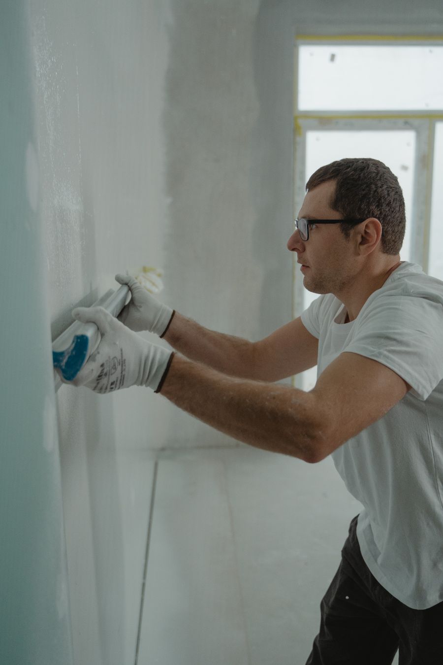 Worker in gloves smoothing joint compound over a drywall seam