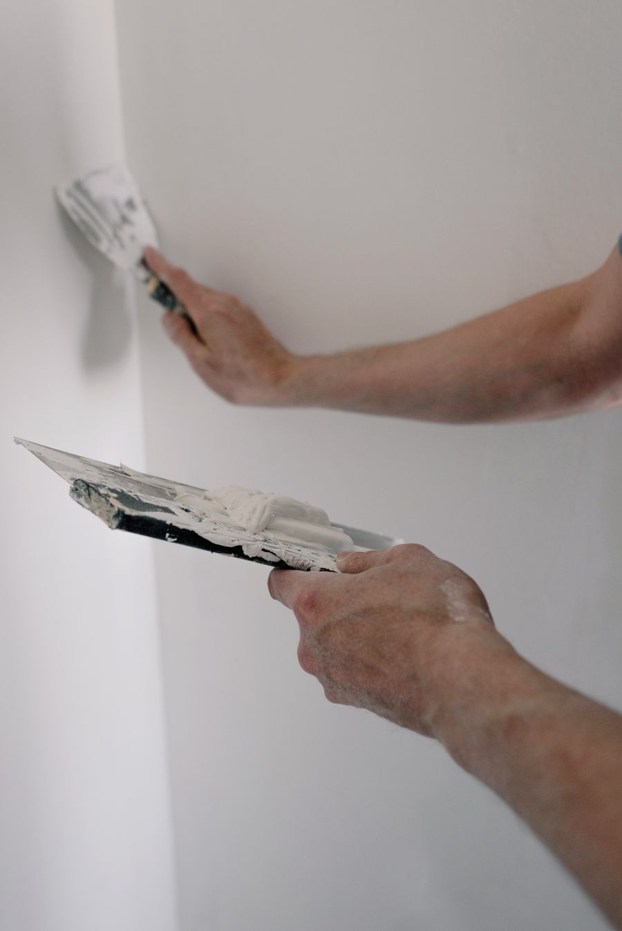 Hands holding trowels loaded with wall compound beside a finished wall