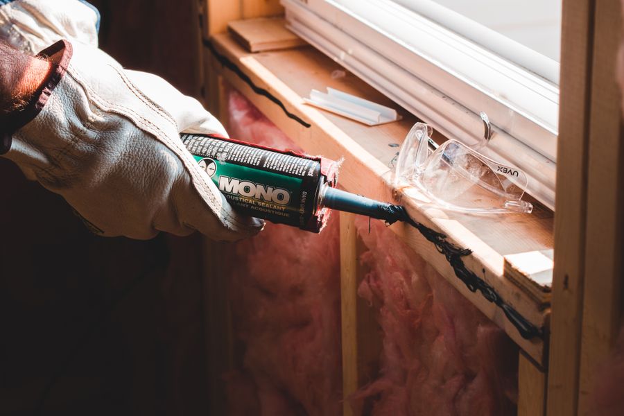 Gloved hand sealing a window seam during weatherization work