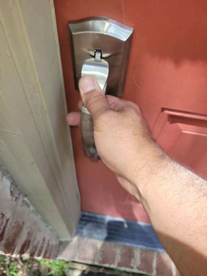 Technician fitting a brushed-nickel handleset on a red entry door
