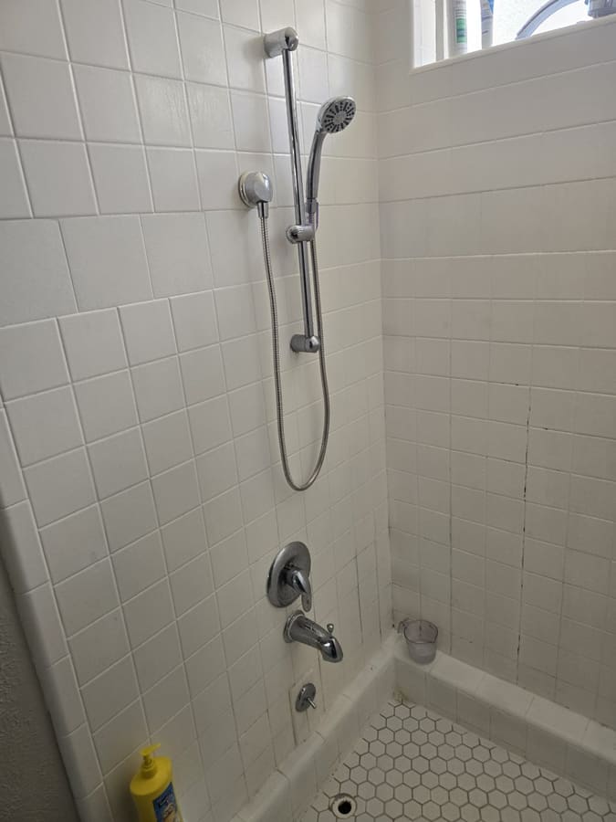 White tiled shower with a new chrome slide-bar hand shower
